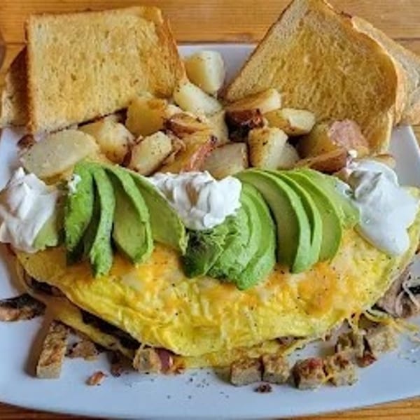 A fluffy omelet topped with avocado slices and sour cream, served with toast and roasted potatoes.