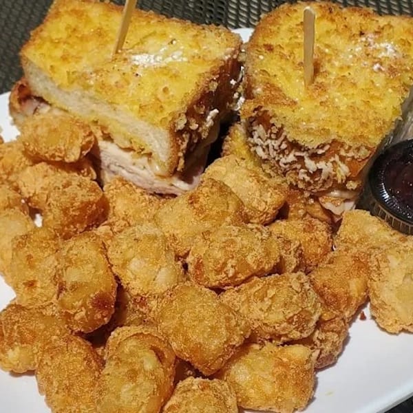 Two golden-brown Monte Cristo sandwiches with a side of tater tots and a dipping sauce.