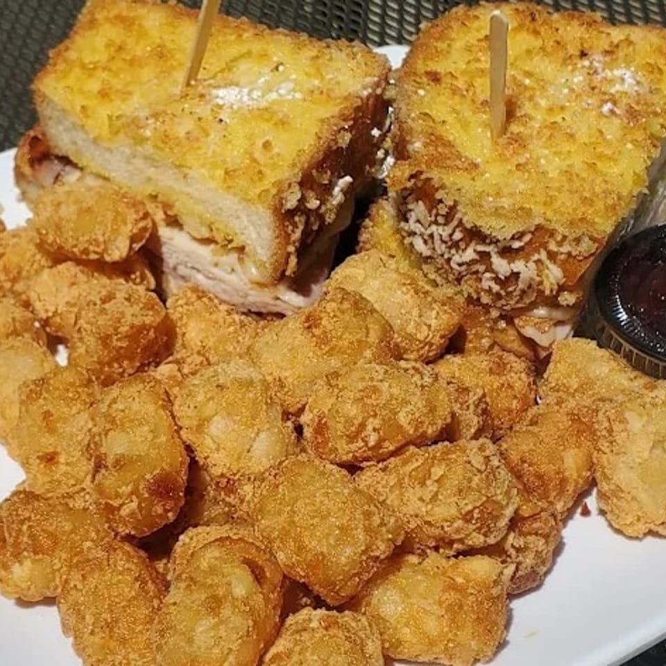 Two golden-brown Monte Cristo sandwiches with a side of tater tots and a dipping sauce.