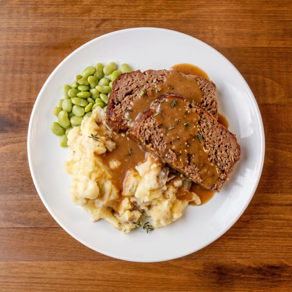 Meatloaf slices with gravy, mashed potatoes, and lima beans on a white plate.