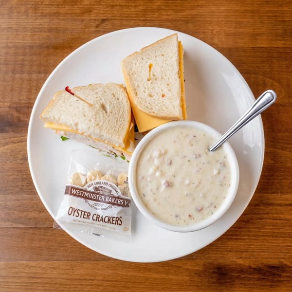 Overhead view of a turkey and cheese sandwich, clam chowder, and oyster crackers on a white plate.