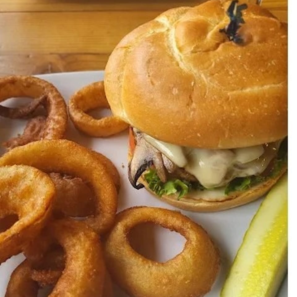A mushroom swiss burger with lettuce and tomato, served with onion rings and a pickle spear.
