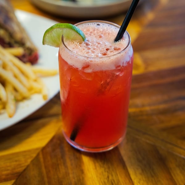 A vibrant red cocktail with a lime wedge and black straw, next to a plate of fries.