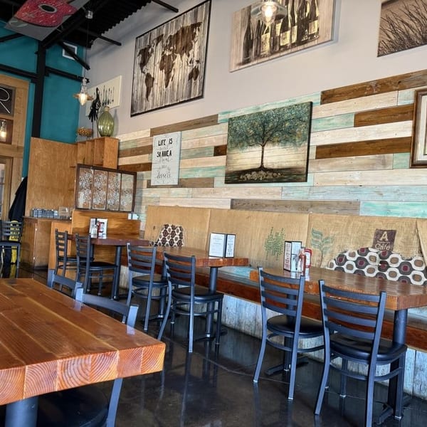 Restaurant interior with wooden tables, black chairs, and a wall decorated with reclaimed wood and art.