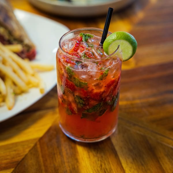 Strawberry mojito with lime and straw, next to a plate of fries and steak.