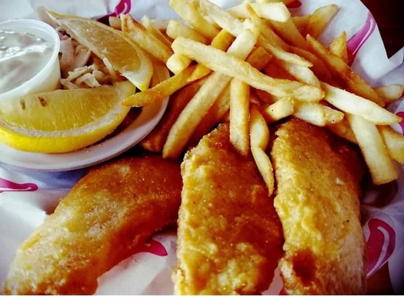 Crispy fish and chips with lemon wedges and tartar sauce in a paper-lined basket.