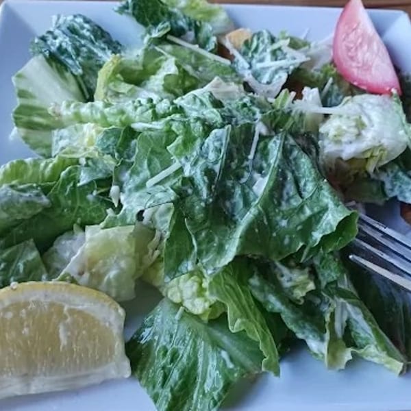 Fresh Caesar salad with romaine lettuce, dressing, a lemon wedge, and tomato slice.