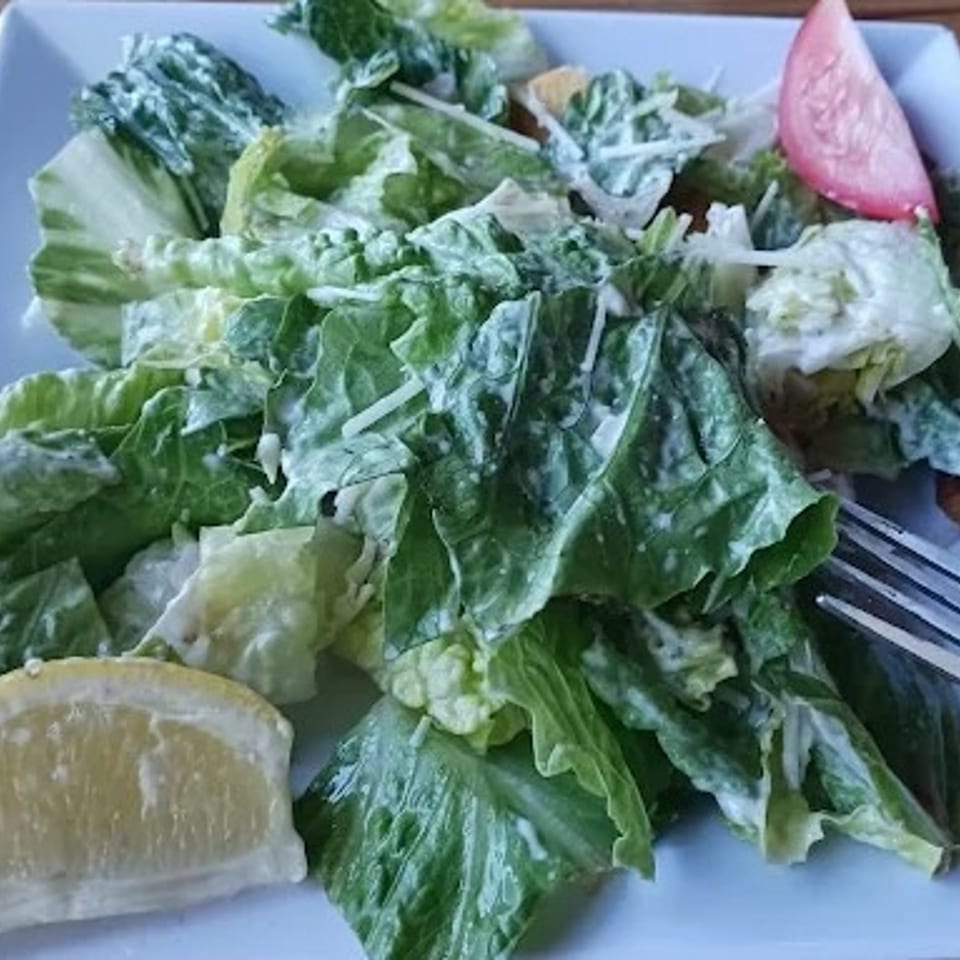 Fresh Caesar salad with romaine lettuce, dressing, a lemon wedge, and tomato slice.