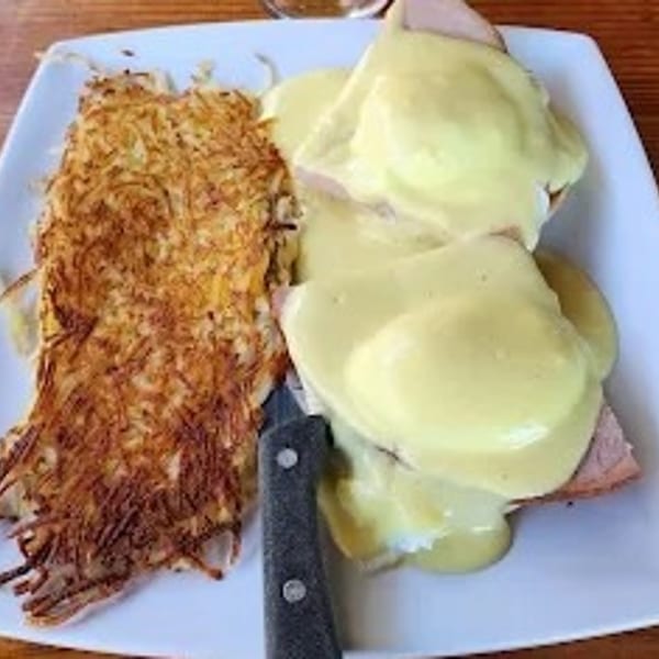 Eggs Benedict with hollandaise sauce and a side of crispy hash browns on a white plate.