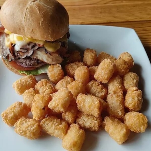 A burger with cheese, bacon, and mushrooms, served with a side of golden tater tots.