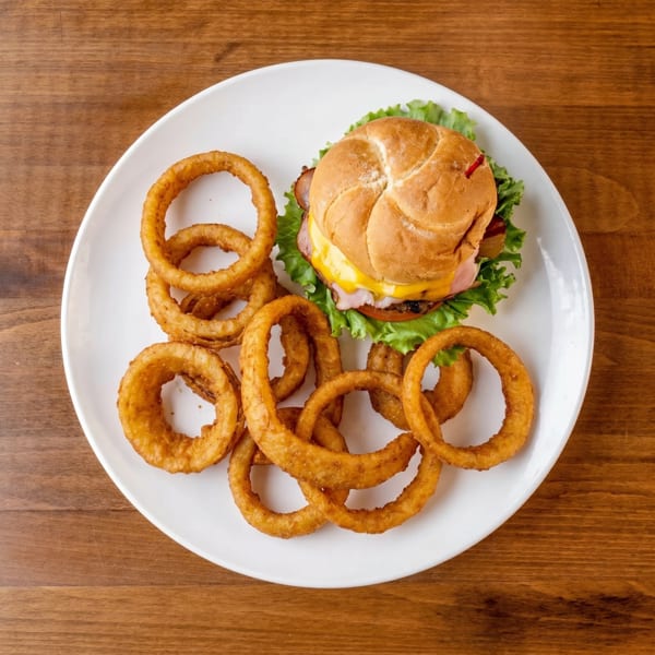 Top-down view of a burger with cheese, lettuce, and tomato, served with a pile of onion rings.