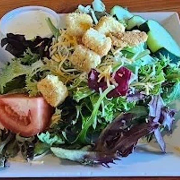 A fresh garden salad with lettuce, tomatoes, cheese, croutons, and a side of ranch dressing.
