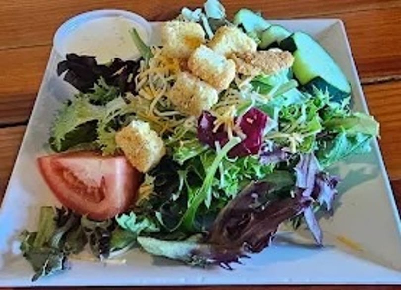 A fresh garden salad with lettuce, tomatoes, cheese, croutons, and a side of ranch dressing.