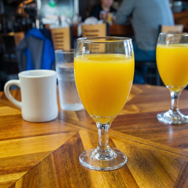 Two glasses of orange juice, a water glass, and a white mug on a wooden table.
