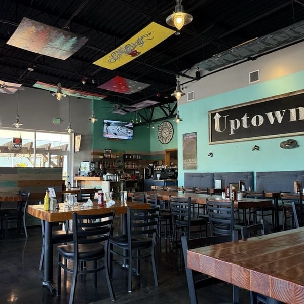 Spacious, modern restaurant interior with wooden tables, black chairs, and a large "Uptown" sign.
