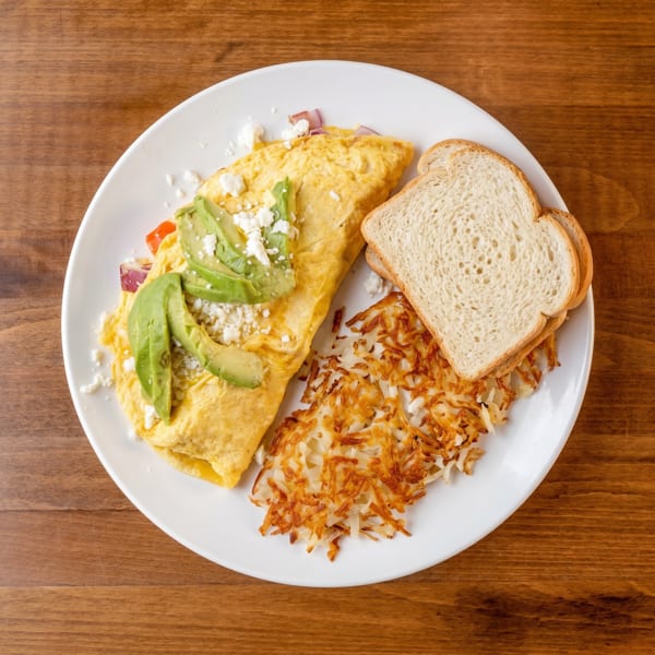 Omelet with avocado, feta, and red onion, served with hash browns and toast on a white plate.