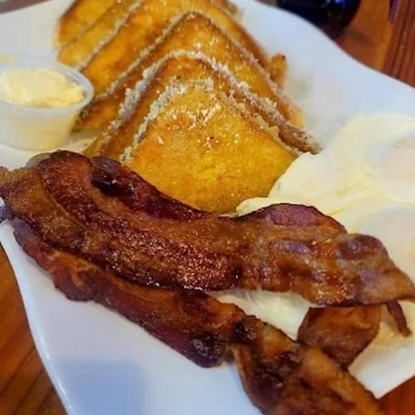 Breakfast plate with French toast, crispy bacon, scrambled eggs, and a side of butter.