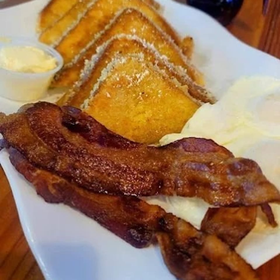 Breakfast plate with French toast, crispy bacon, scrambled eggs, and a side of butter.