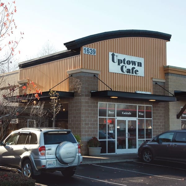 Exterior view of Uptown Cafe, a brick and wood-paneled building with parked cars in front.